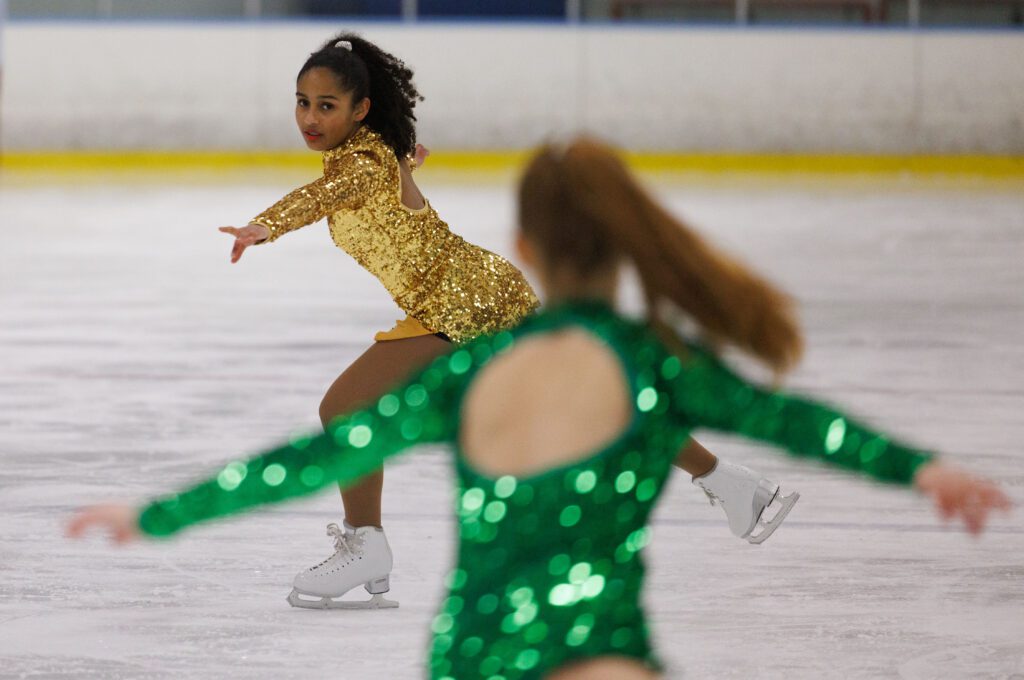 Coco Overstreet, wearing yellow, looks to her partner Carolina Kovacevic as they practice as they take their positions and poses on the ice rink.