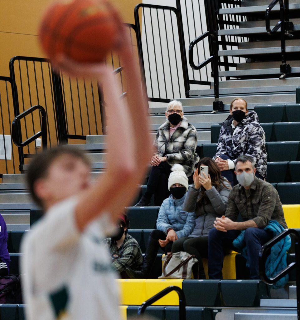 A player takes a shot for the basket as spectators waearing masks watch from the bleachers.