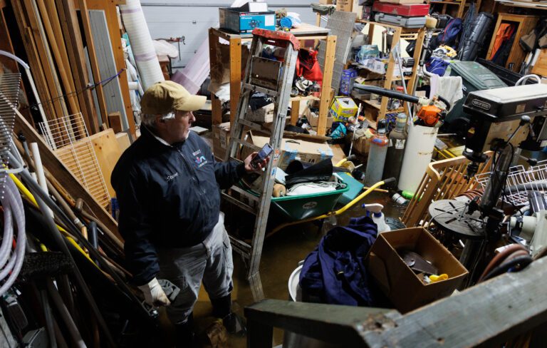 Steve Wight chuckles as a weather alert shows up on his cell phone while walking in his flooded garage on Dec. 28 in Sandy Point.