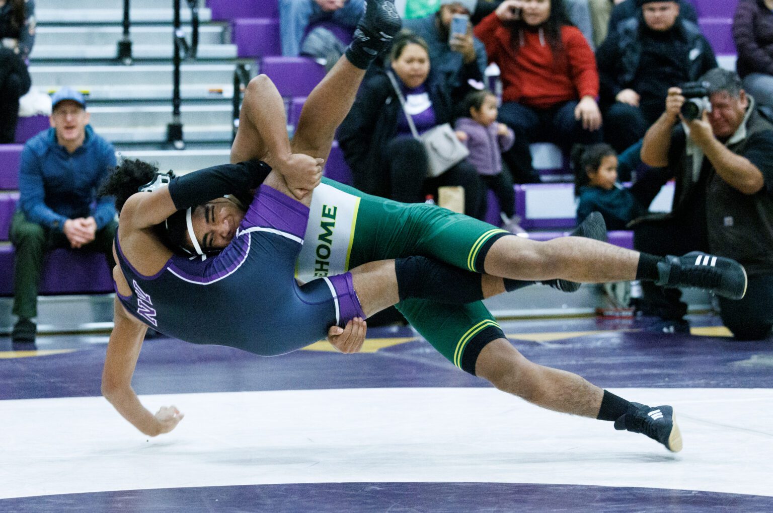 Sehome’s Pierson Lewis throws Nooksack Valley’s Gio Coleman to the mat as a crowd of spectators and photographers watch from the sidelines.