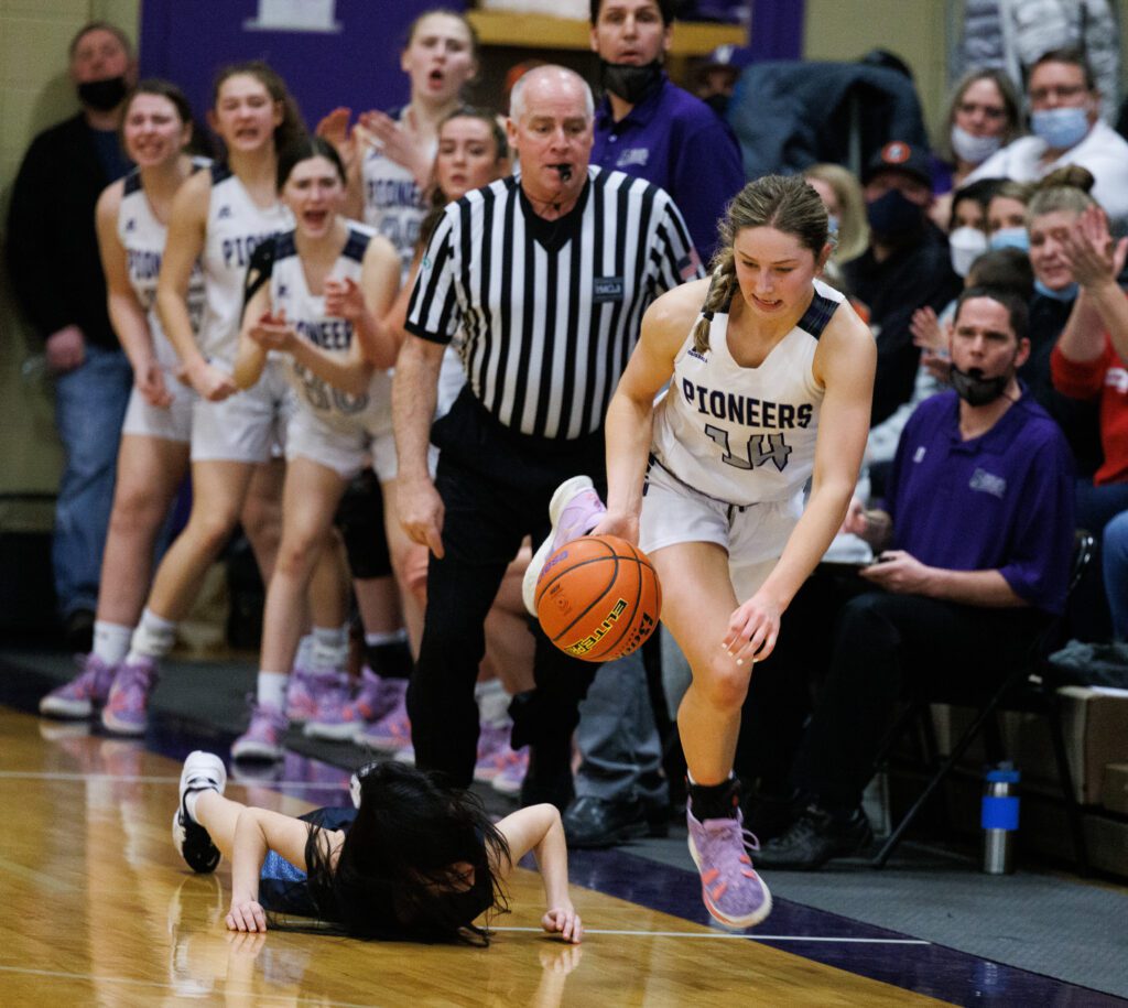 Nooksack Valley's Devin Coppinger stumbles over Lynden Christian's Daisy Poag as a referee watches closely next to the cheering sidelines.