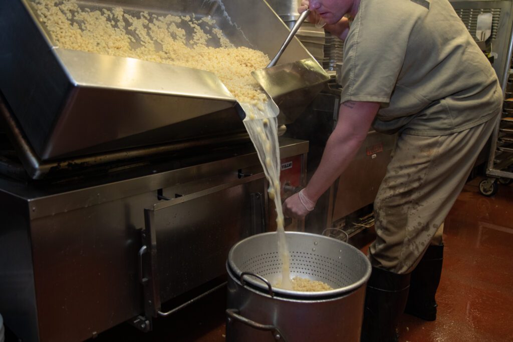 An inmate drains a vat of cooked pasta into a strainer that drains into a big pot underneath.