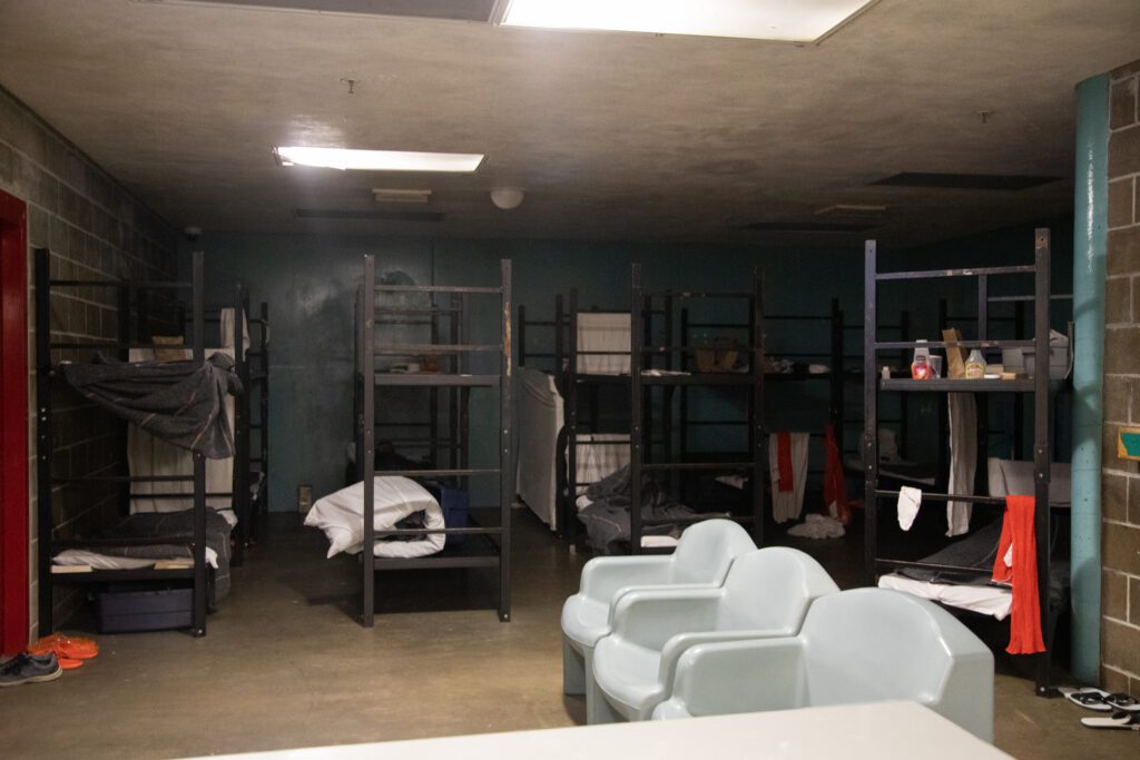 Five metal bunkbeds crowd a dark room in a jail.
