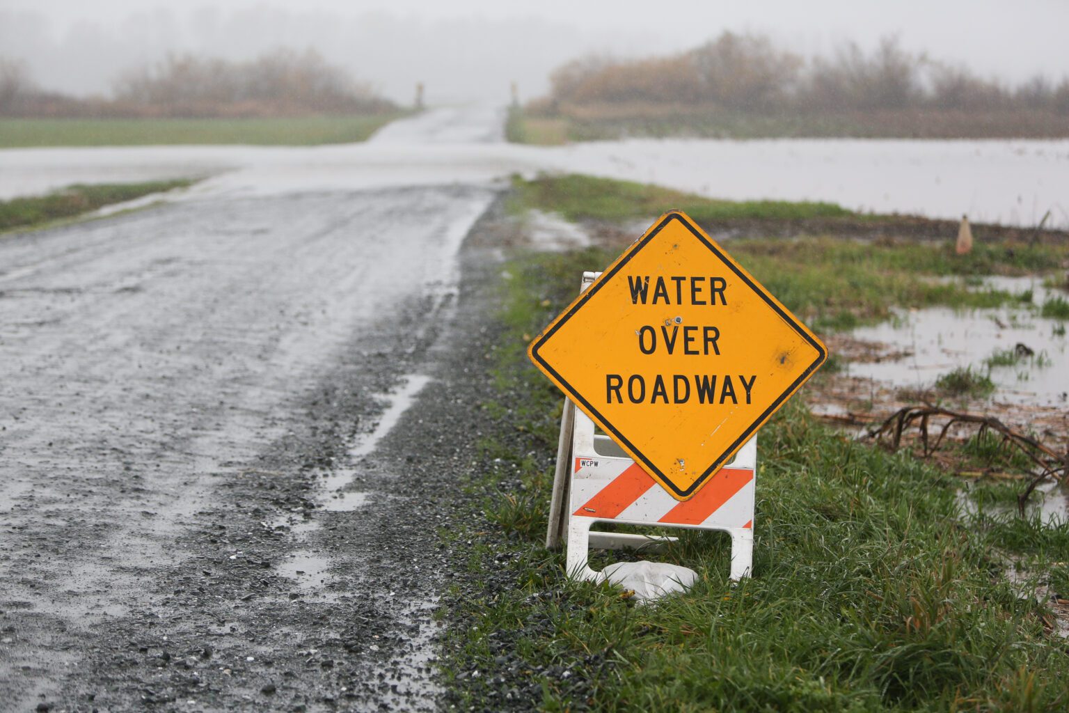 Floodwaters cover a road in Lynden as a yellow sign is placed in the grass warning the drivers of water over roadway.