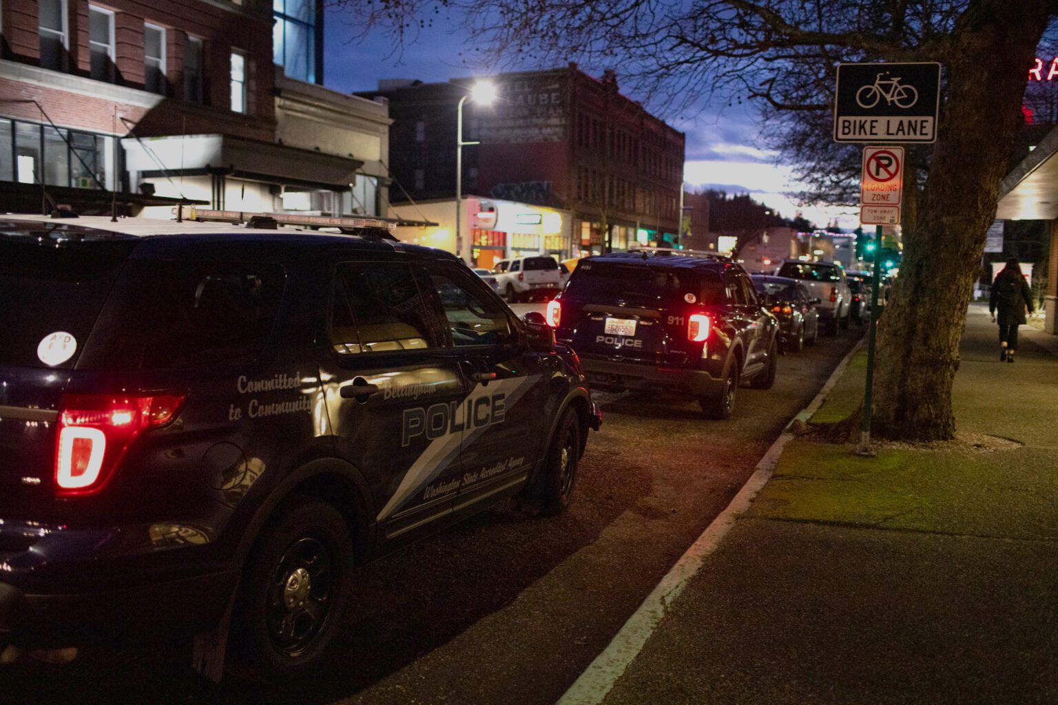 Bellingham Police Department cars are parked along a downtown street in the evening.