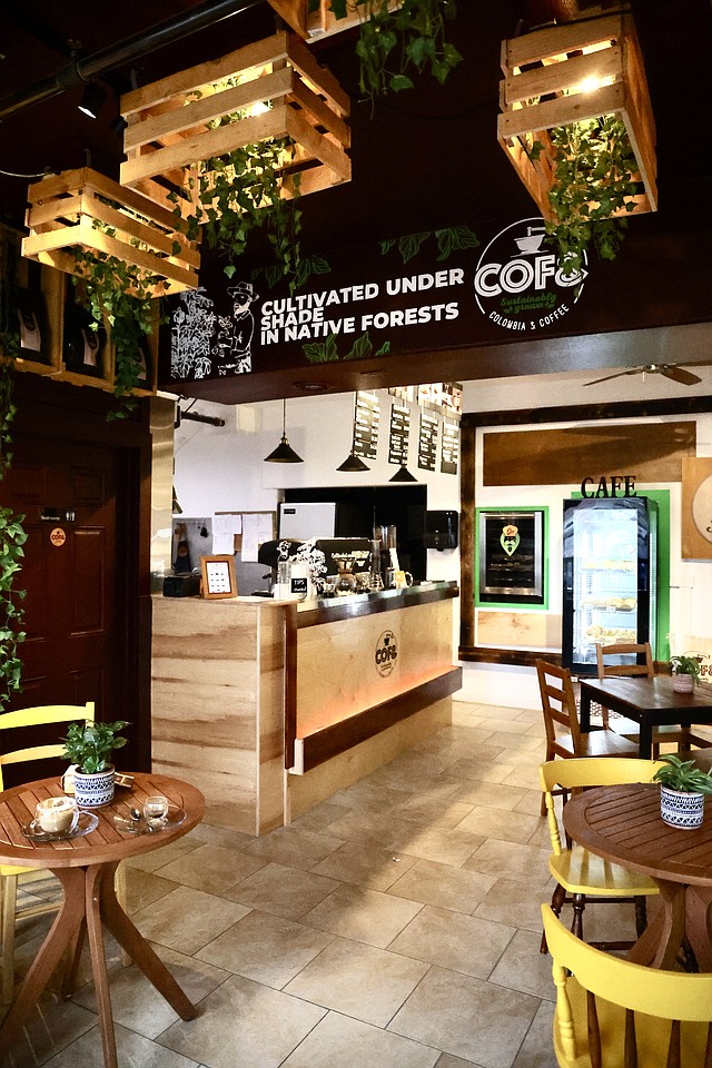 The interior of a coffee shop has plants hanging from the ceiling.
