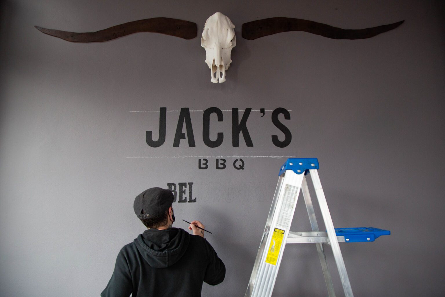 Kitchen manager Colby Fowler paints the Jack's BBQ logo on the wall of the restaurant on Feb. 16. Fowler
