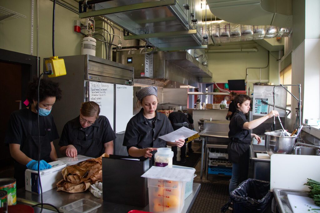 Workers wearing black look at prep lists in a professional kitchen.