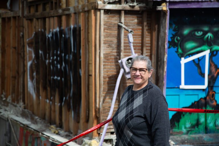 Fourth Corner Frames & Gallery owner Sheri Wright stands in front of the damaged wall to her building on Holly Street on April 15.