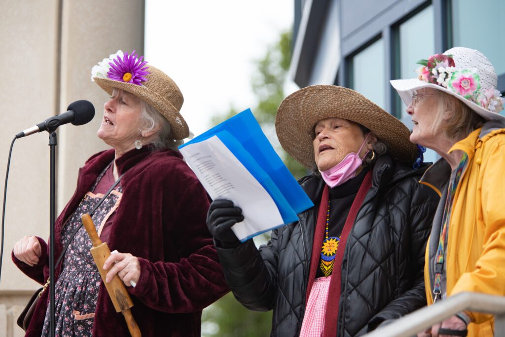 From left, Raging Grannies Kathy Leathers, Graciela Luna and Susie Bradley sing 'Roe, Roe, Roe v. Wade." All wearing straw hats with flowers decorating the top as they hold up lyrics to the song.