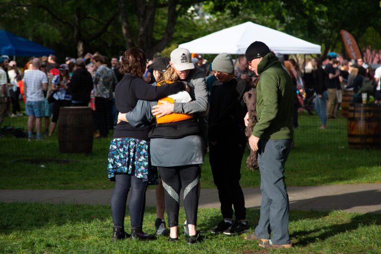 Dawn Groves and friends hug, after learning the news of her teammate's death while on the Ski to Sea course as a crowd unknowingly celebrate behind them.