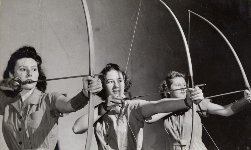 A vintage photo of three women each drawing their bow and arrow.