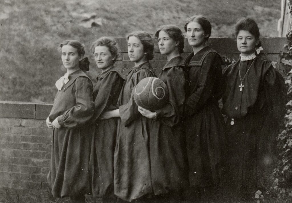 Six women pose in a row while holding a basketball.