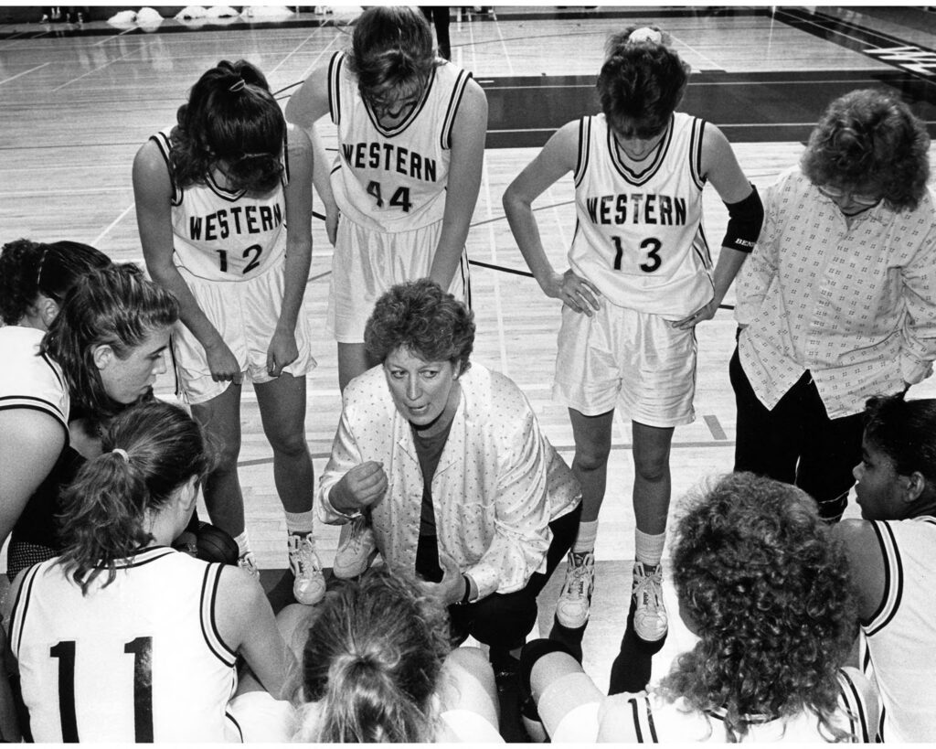 A vintage photo of a coach surrounded by her basketball team consisting of all women.
