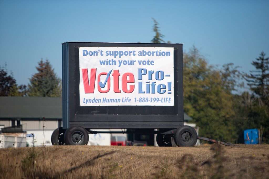 A pro-life sign banner sits off of the Guide Meridian with details of their phone contact number.