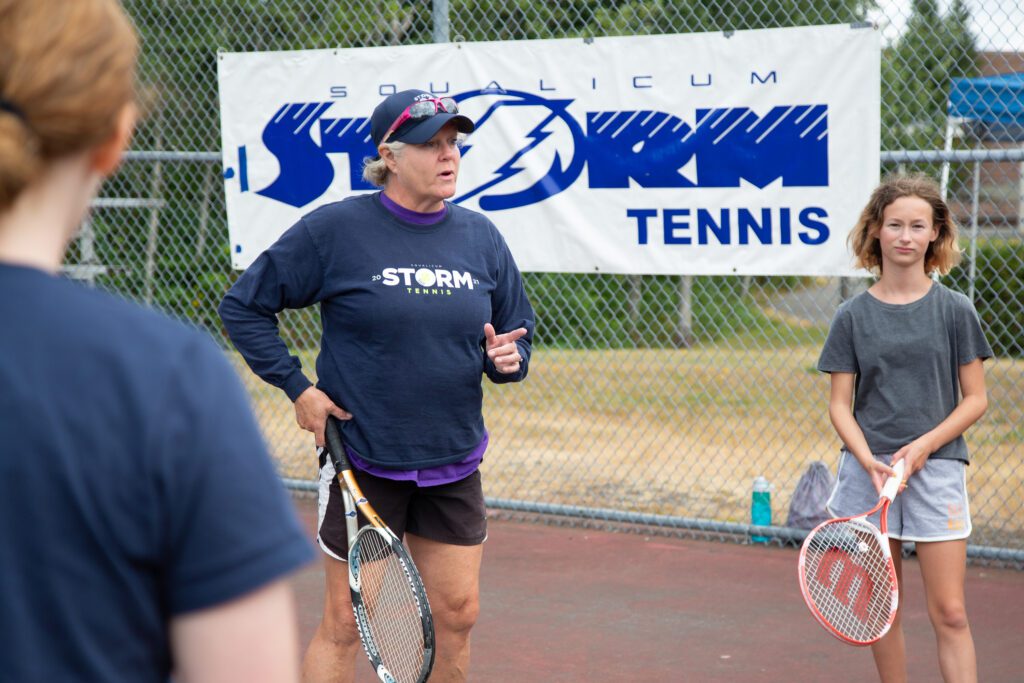 Angie Harwood coaching younger athletes in front of the Storm Tennis banner.