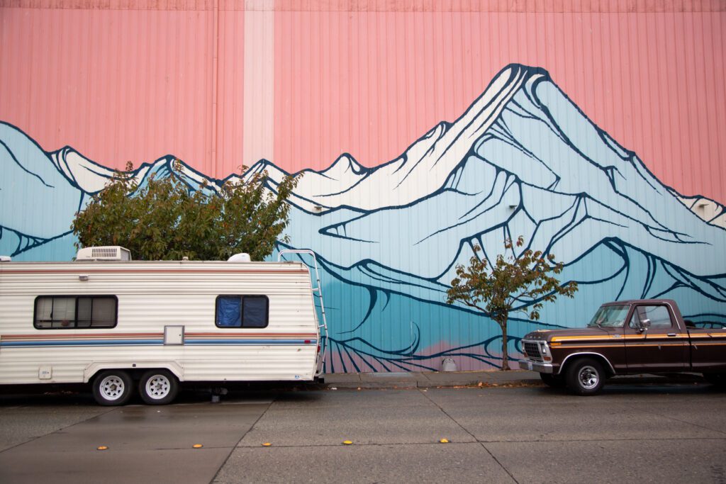 An RV and truck are parked alongside a mural of a mountain.