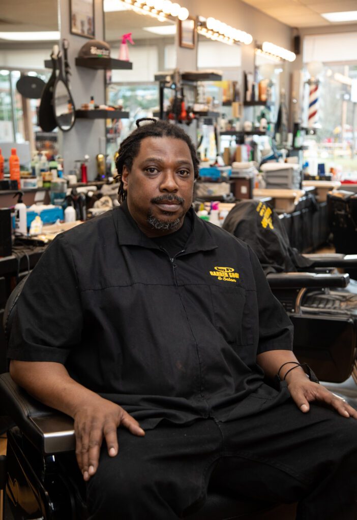 Bernard Franklin sitting on one of the barbershop's chairs inside his shop.
