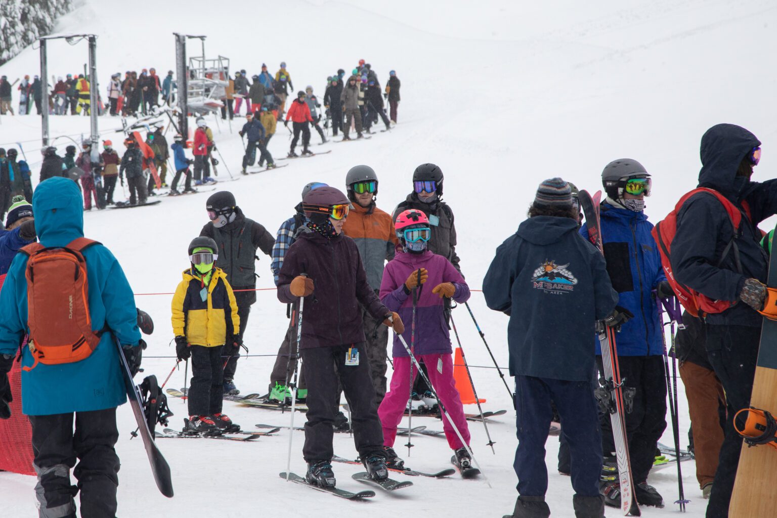 Dozens of people line up with their snowboards and skis dressed in a multitude of colored winter gear and visors.
