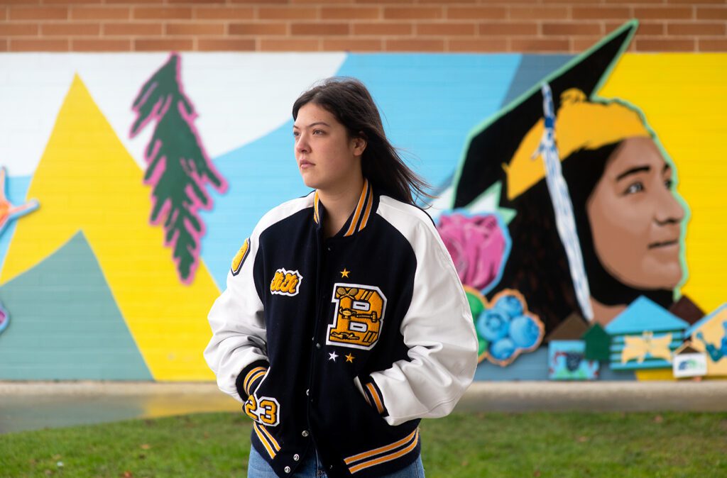 GiGi Searle, a Burlington-Edison High School senior stands in front of one of her peer's memorial while wearing her school's varsity jacket.