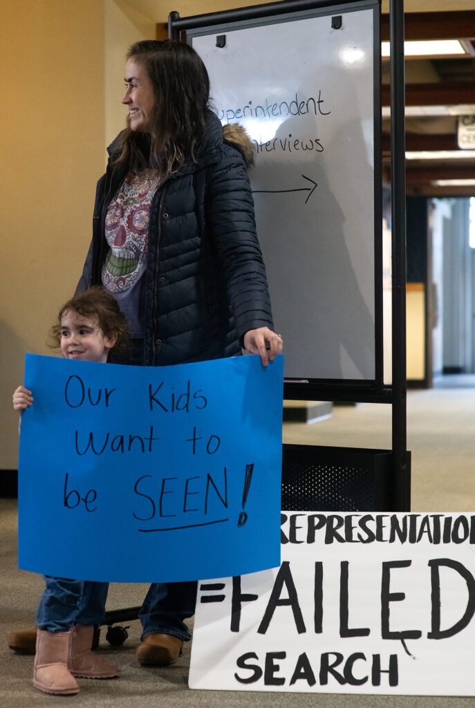 Mariana Carroll and her 3-year-old daughter, Lucia, hold up a blue and white sign in protest of the superintendent decision.