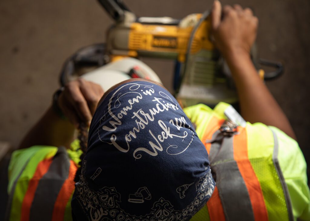 Top view of a woman's head, her blue bandana reads : Women in Construction Week.