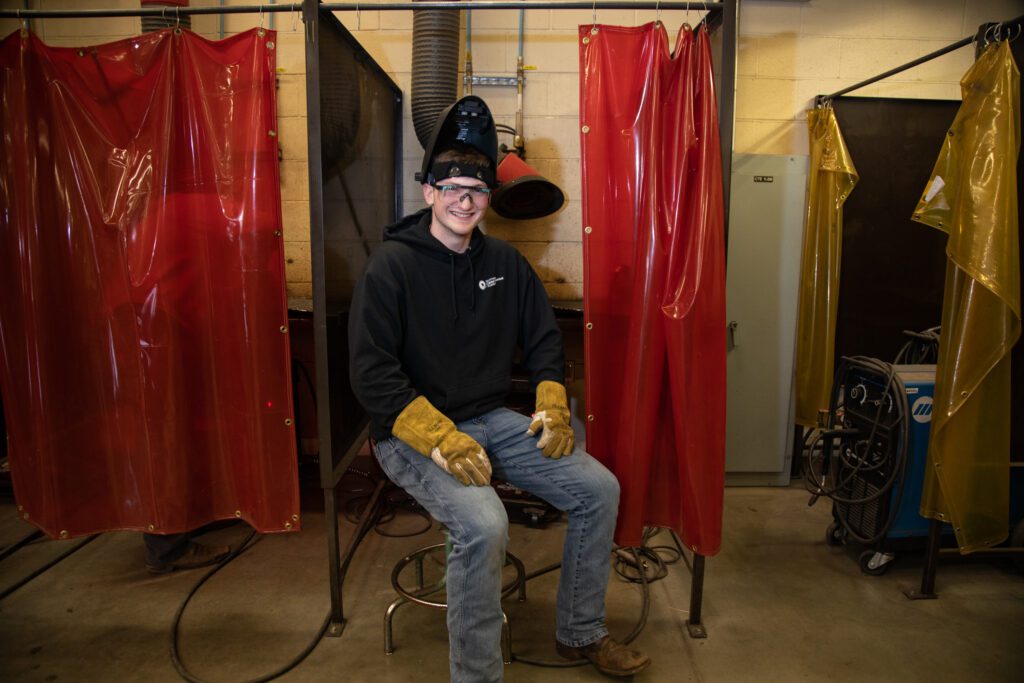 Blaine High School senior Trevor Goltz sitting on a stool while wearing welding protective gear.