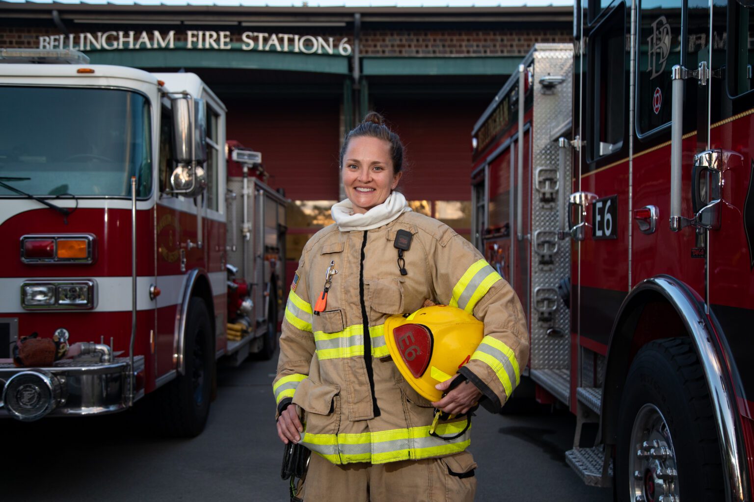 Rebecca Pederson donning on her firefighter gear and posing inbetween two firetrucks.