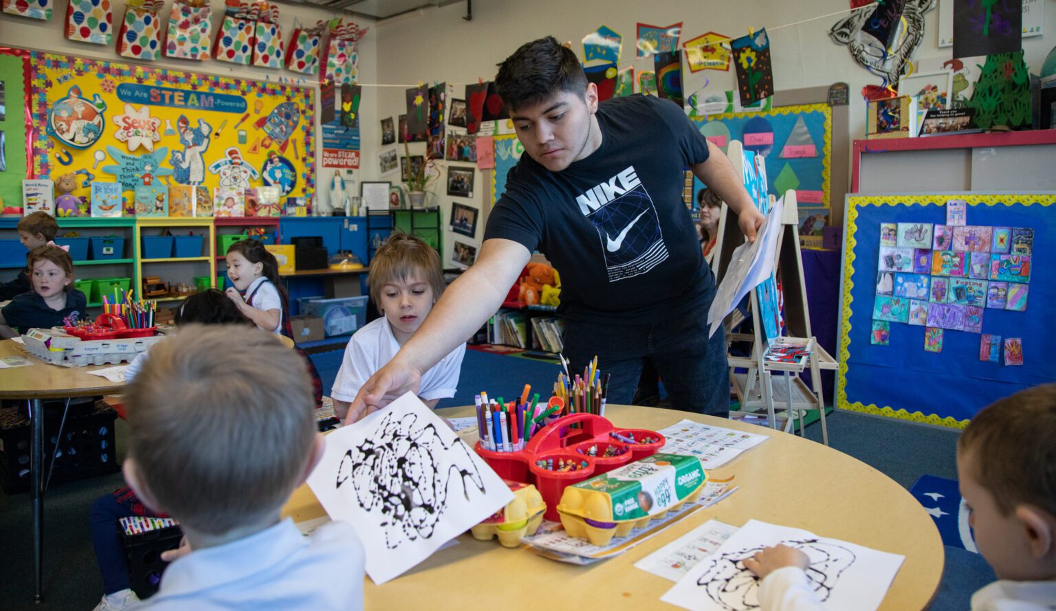Bellingham High School senior Ivan Gomez passes out scribble paper to kindergartners March 28 at Assumption Catholic School. Gomez interns with the class two mornings a week as part of the Bellingham Public Schools Teacher Academy