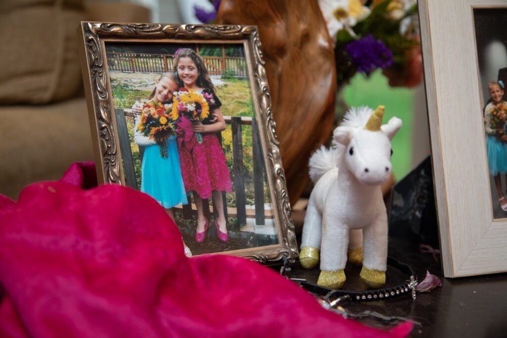 A framed photo of Emily Halasz and her friend holding a bouquet of flowers as other trinkets surround the photo frame like a white unicorn stuffed toy and a bracelet.