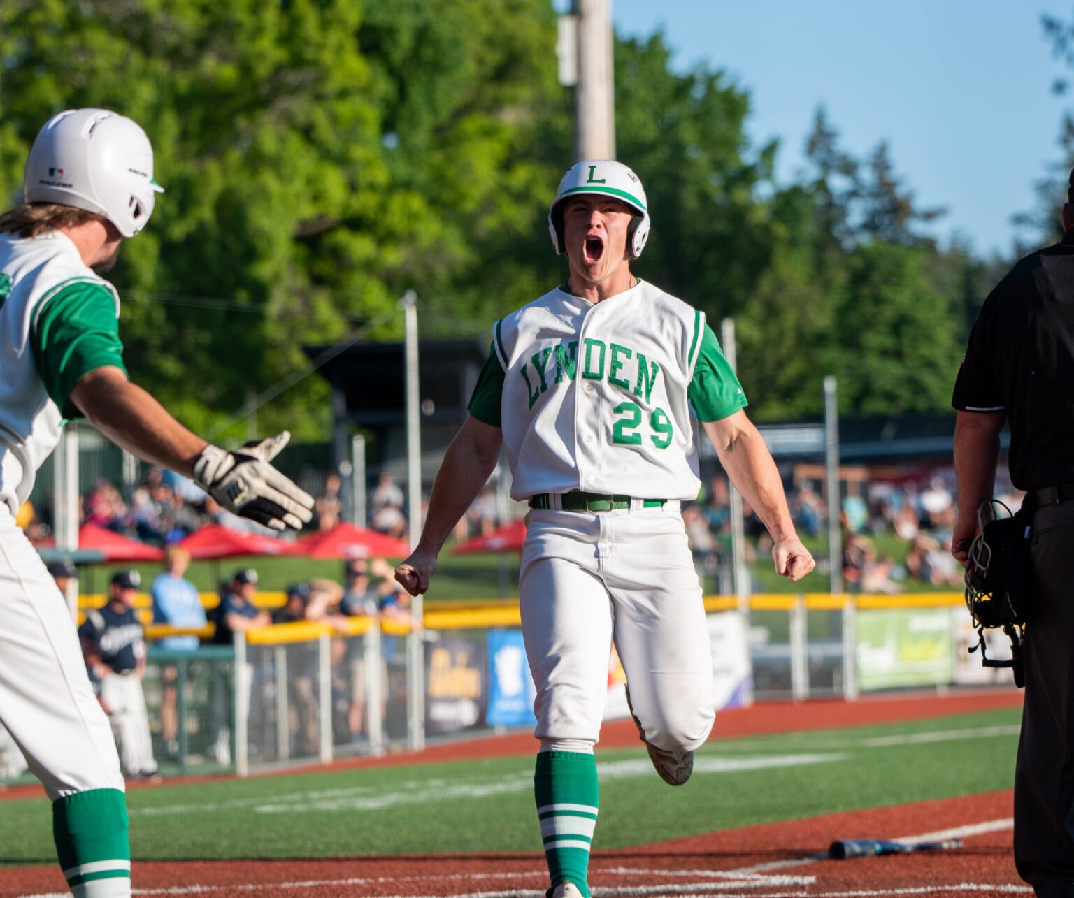 Lynden senior outfielder Campbell Nolte yells in celebration after crossing home plate as his teammate runs up to him from the side.