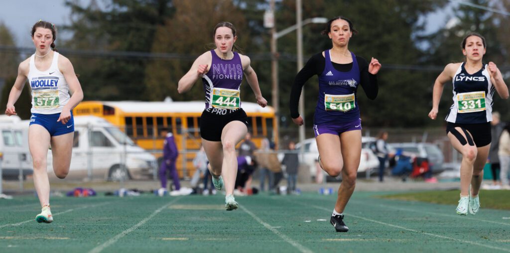 Nooksack Valley's Kate Desilets runs alongside other track runners as spectators watch near the fences far behind them.