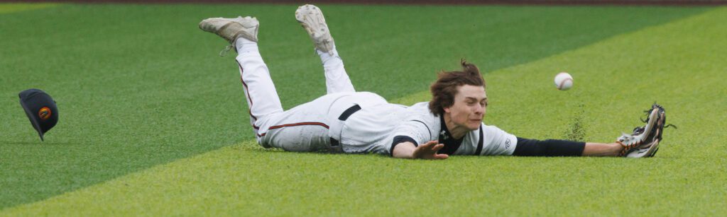 Blaine’s Jesse Deming dives and slides against the floor with his hands spread wide while the ball bounces off the grass beside him.