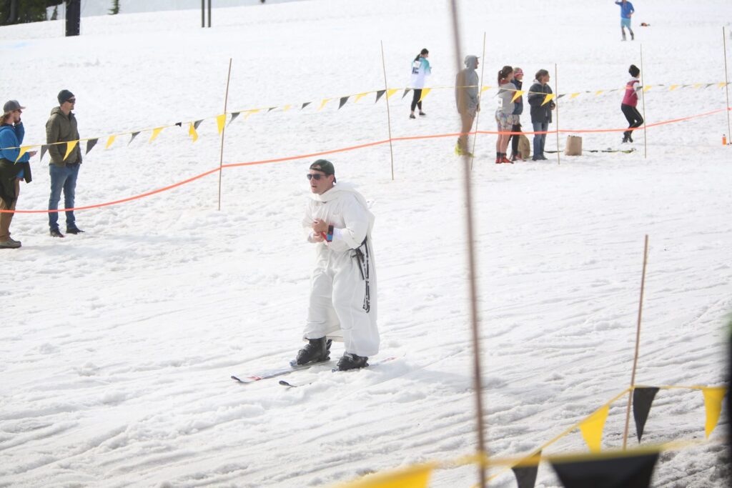 Matt Cooley prepares for the handoff as he finishes the downhill ski/snowboard leg dressed in a white body suit.
