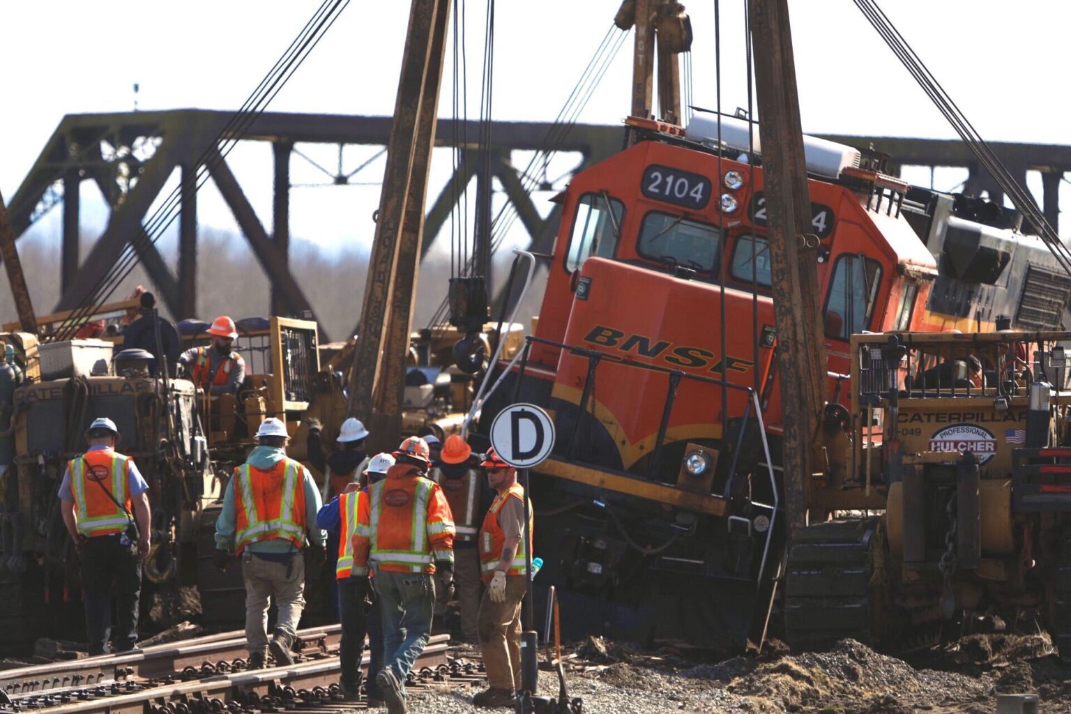 Crews surround an overturned locomotive as others try to put the locomotive back in place on the rails.