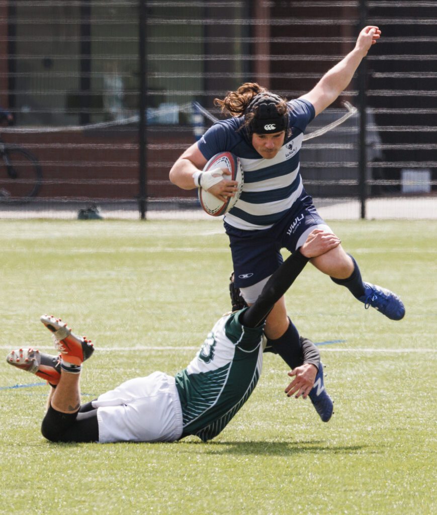 Western Washington University’s Noah Weiss leaps to try and avoid the tackle from another player who had dived and wrapped their arms around his legs.