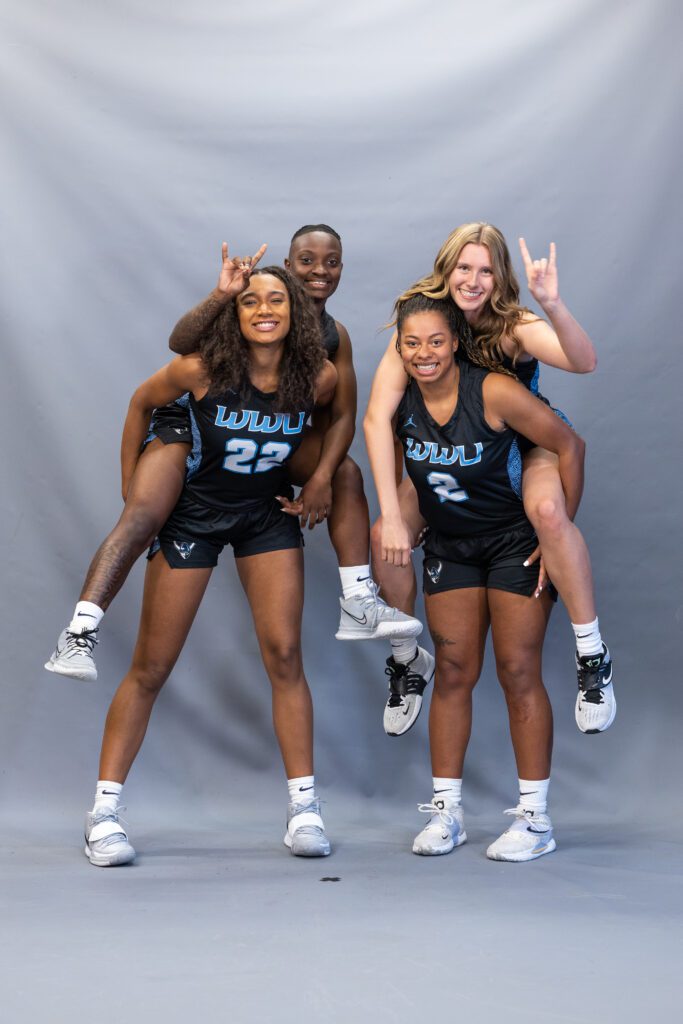 Four basketball players pose for a photo, each pair carrying a player on her back.