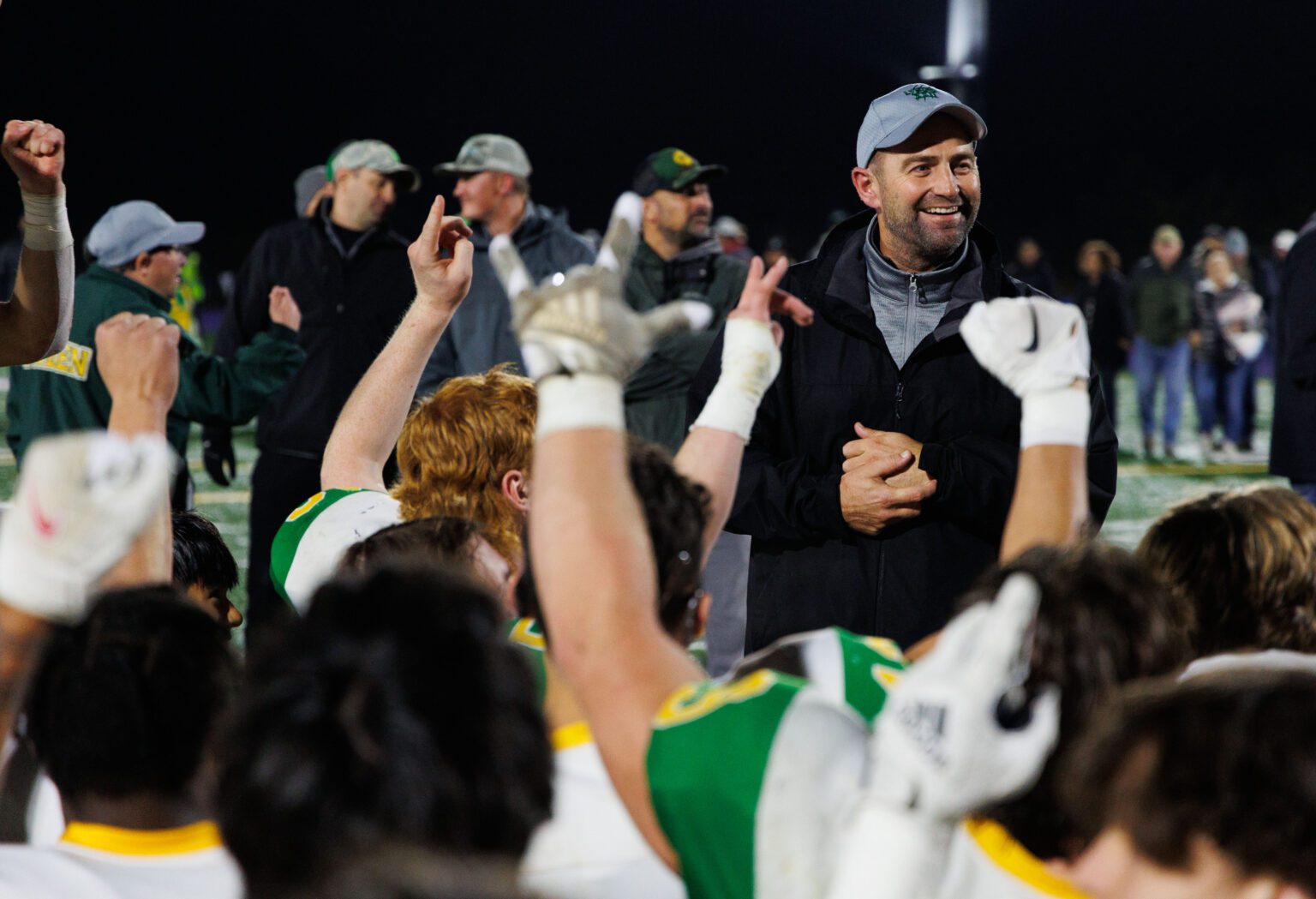 Lynden players cheer with their hands in the air for head coach Blake VanDalen as he smiles at his team.
