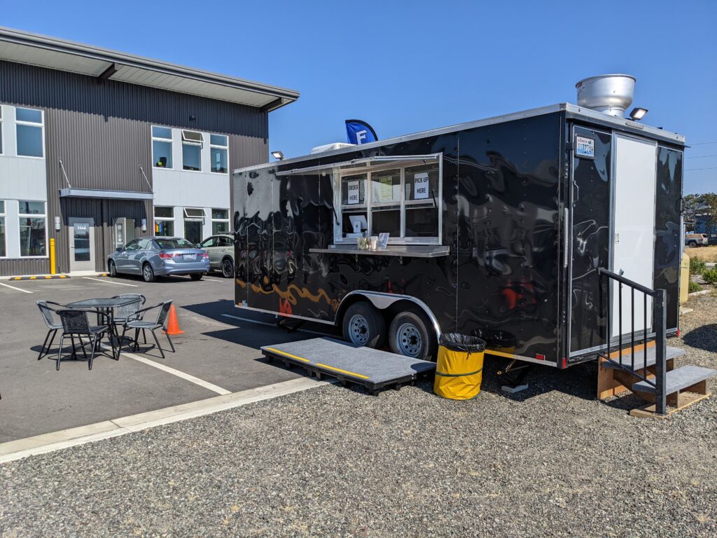The Galley2Go Fish & Chips food trailer with metal tables and chairs next to it.