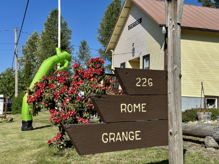 The Rome Grange sign decorated with flowers.
