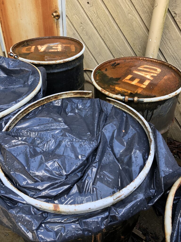 Two barrels labeled, lead, while the other barrels are covered in a black tarp.