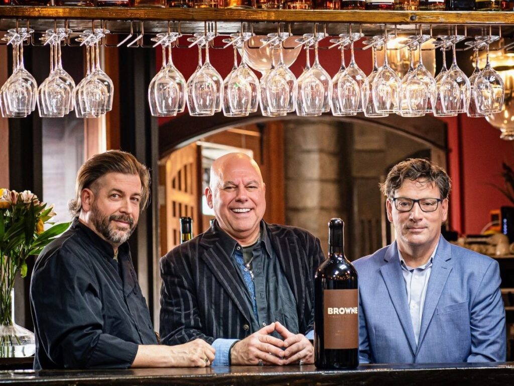 Douglas Elliott (executive chef), Roberto Trendel (managing partner) and Robert Pinkley (owner), from left, pose for a photo underneath rows of wine glasses hanging above the bar.