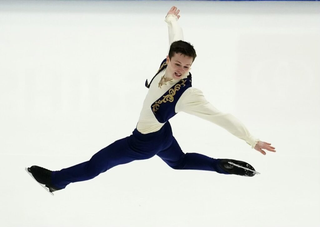 Liam Kapeikis leaps into the air with one leg behind him as he twists his body for a pose.