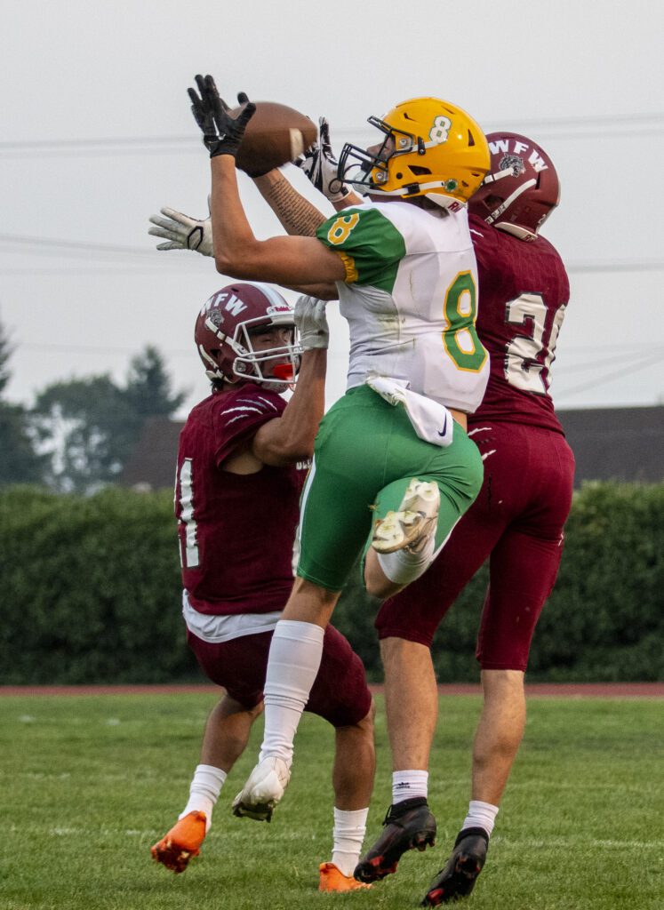 Lynden wideout Isaiah Stanley (8) leaps for a pass while two players from the opposing team reach to stop him.