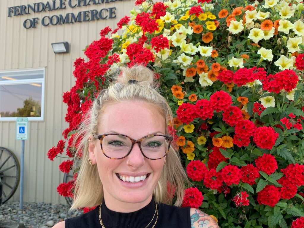 Megan Juenemann smiling for a photo in front of a large bush full of blooming flowers of different colors.