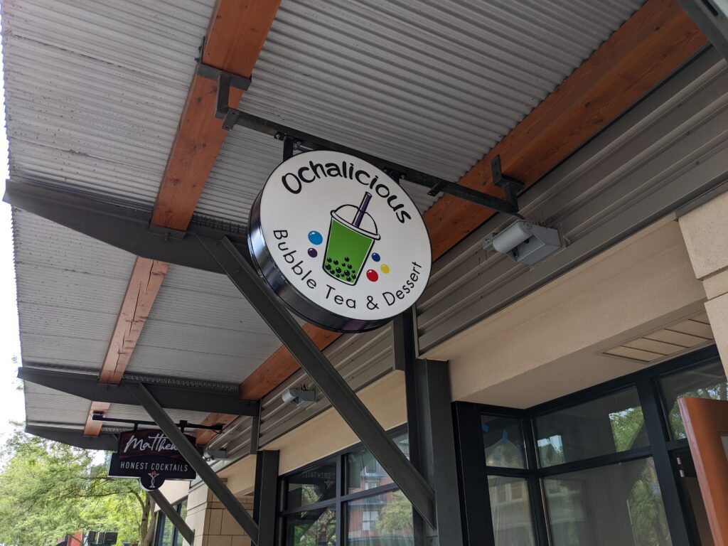 An outdoor sign of Ochalicious Bubble Tea & Dessert showcasing a fun colorful boba drink as a logo.