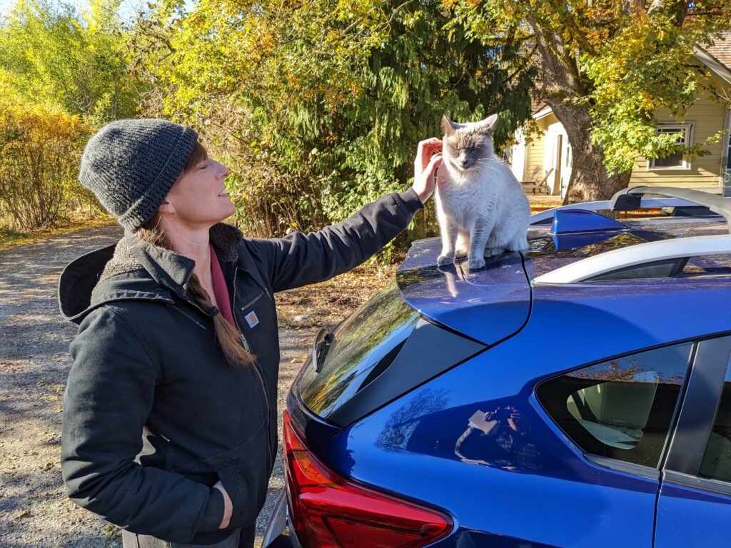 Anna Martin pets Coco, a cat sitting on a blue car.