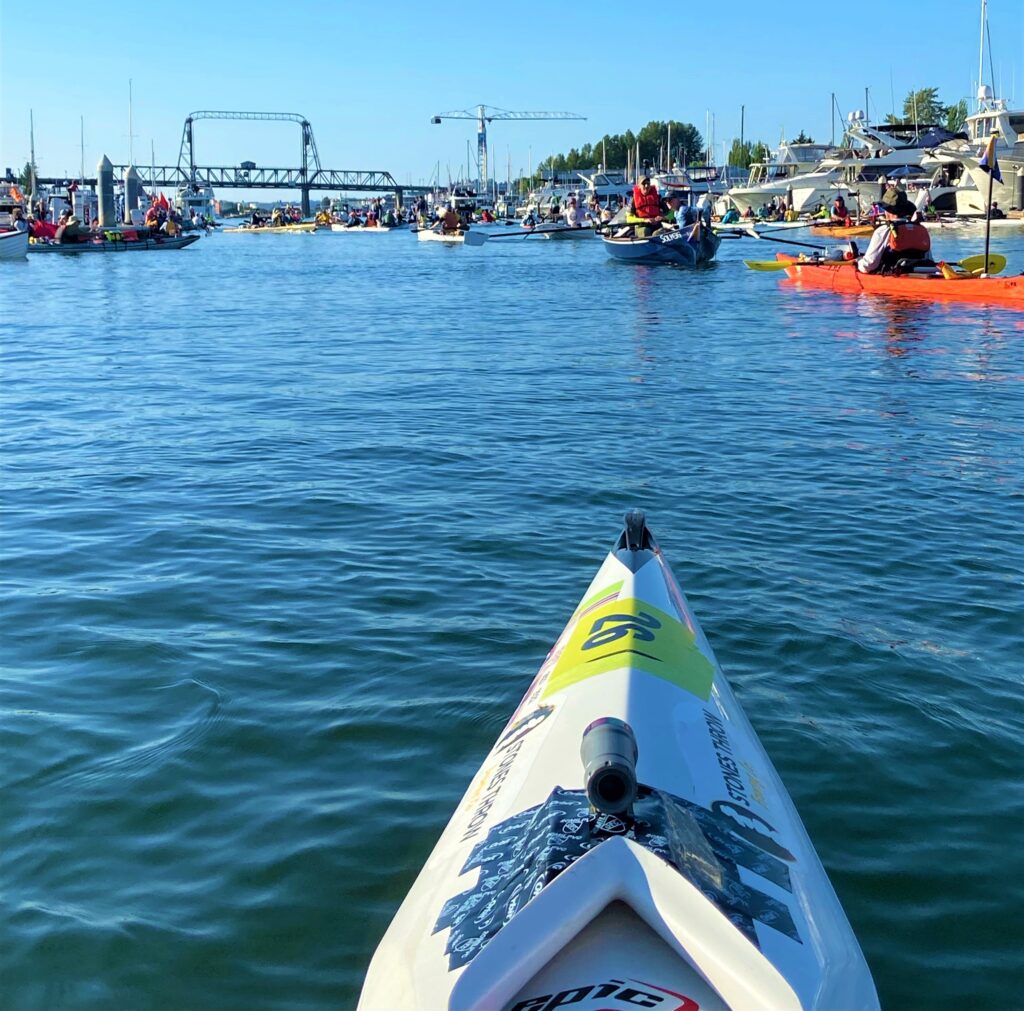 A perspective photo of other kayakers idling in the waters near docked ships.