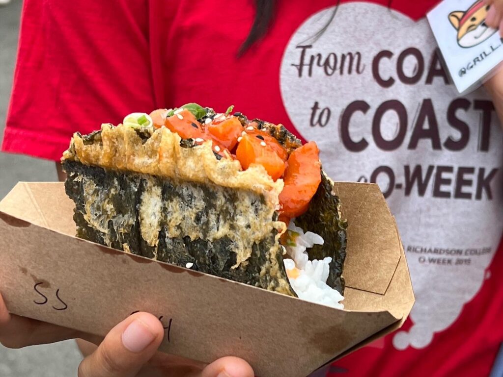 A person holding up a sushi taco where a seaweed is fried to mimic a taco shell filled with salmon, rice and other sushi ingredients.