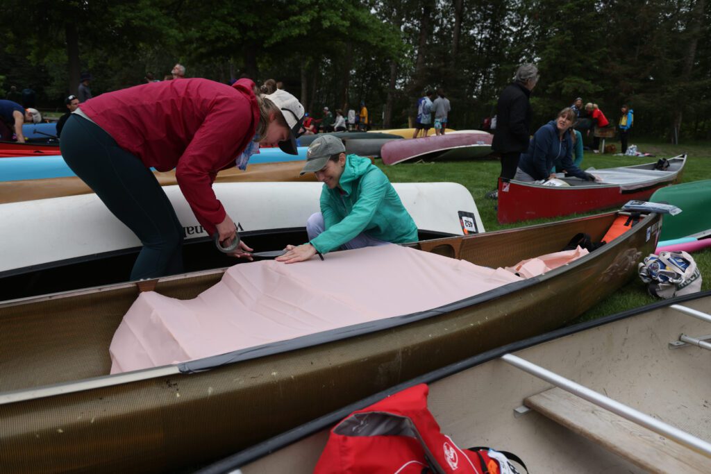 Carolyn Wise, left, and Meadow Didier tape up their canoe while other canoers do the same behind them.